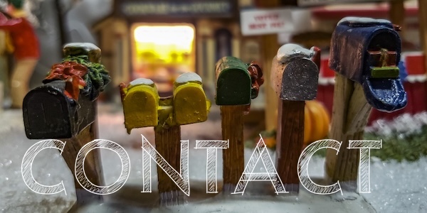 Row of toy mailboxes in front of a group of houses lit up for the holidays